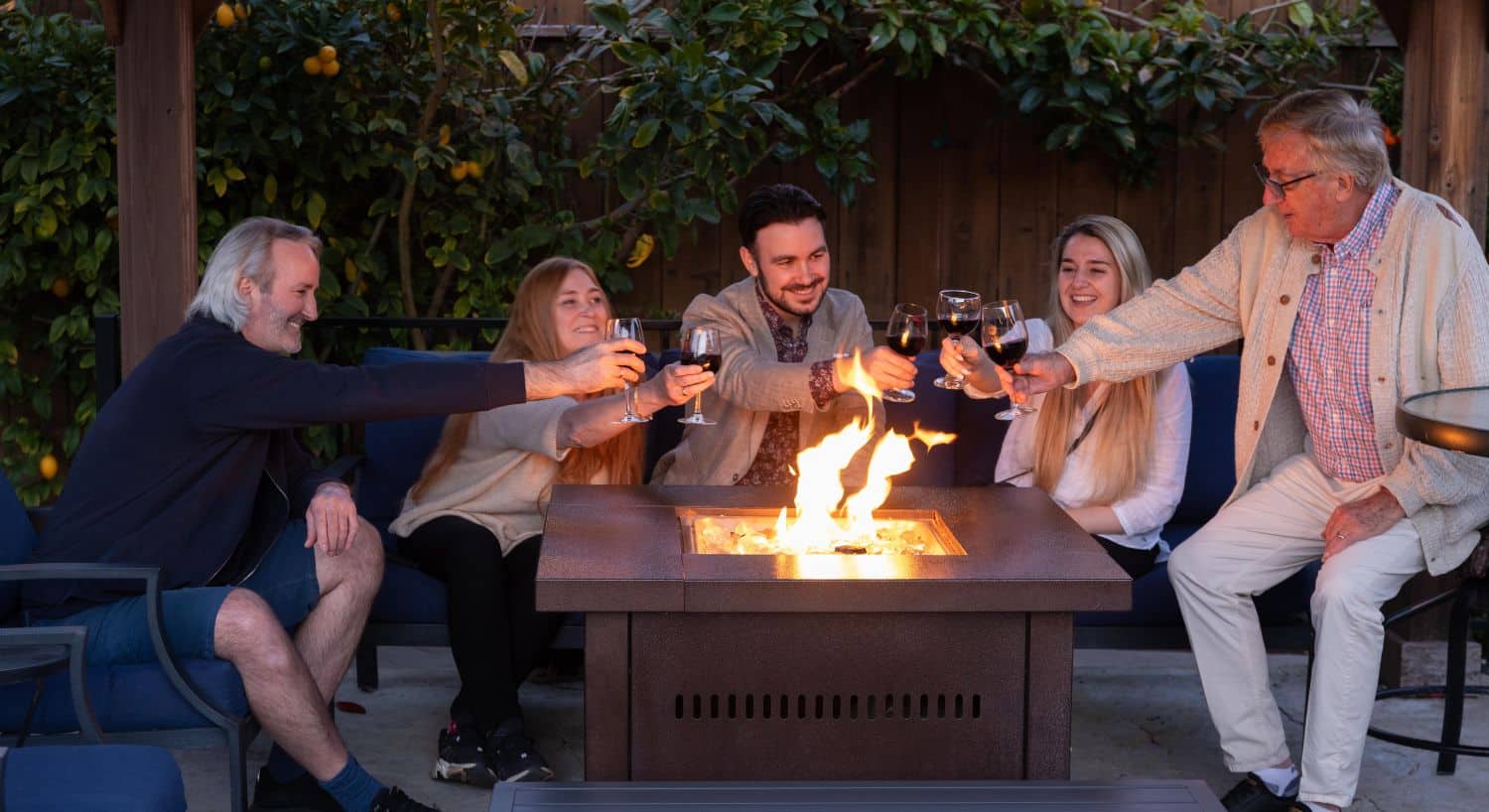 A group of men and women sitting and drinking wine at an outdoor firepit table