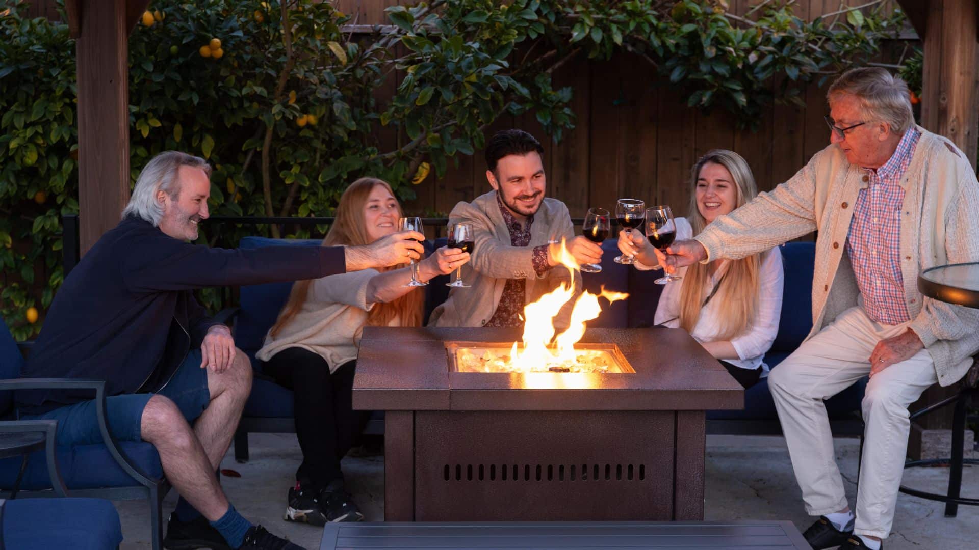 A group of men and women sitting and drinking wine at an outdoor firepit table