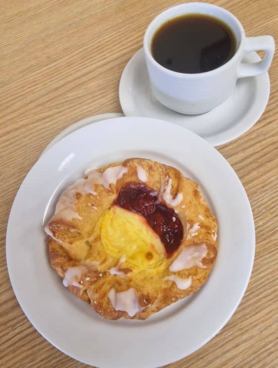 A danish pastry on a white plate next to a mug of coffee
