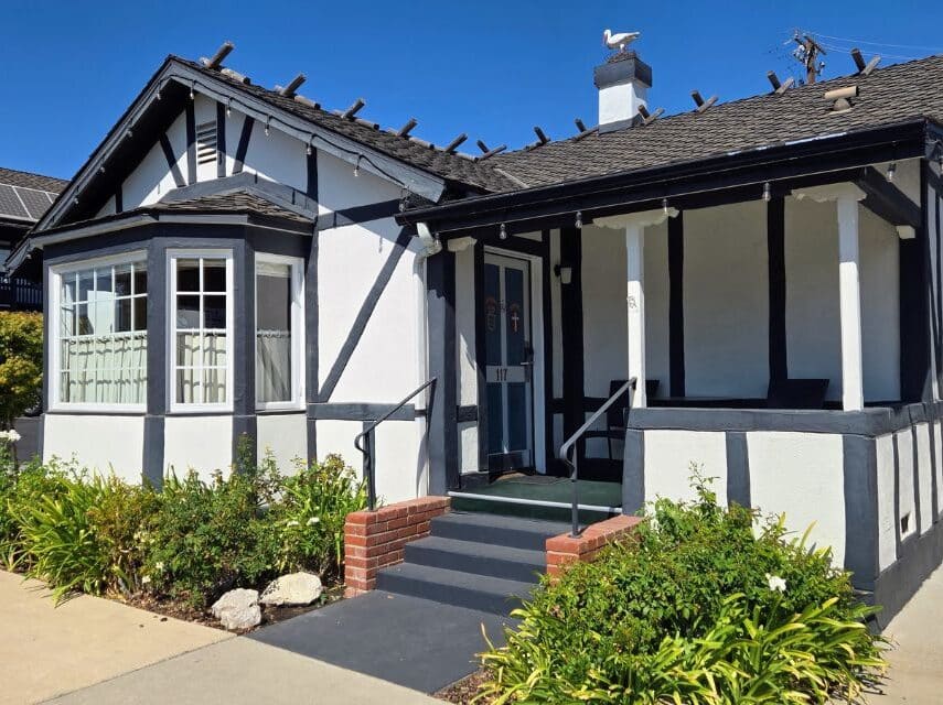 A white cottage with brown trim front steps with green bushes
