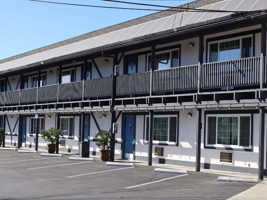 A two story hotel building - white with black trim, blue doors and potted plants.