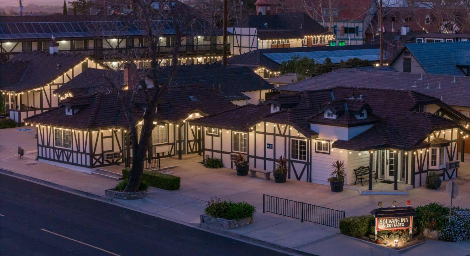 A block of several white buildings with brown trim, an inn, a hotel and cottages, all lit up at night with white lights