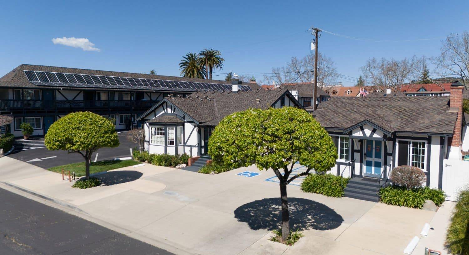 Front sidewalk area by two stand alone white and brown cottages, with two trees and a large hotel building next door