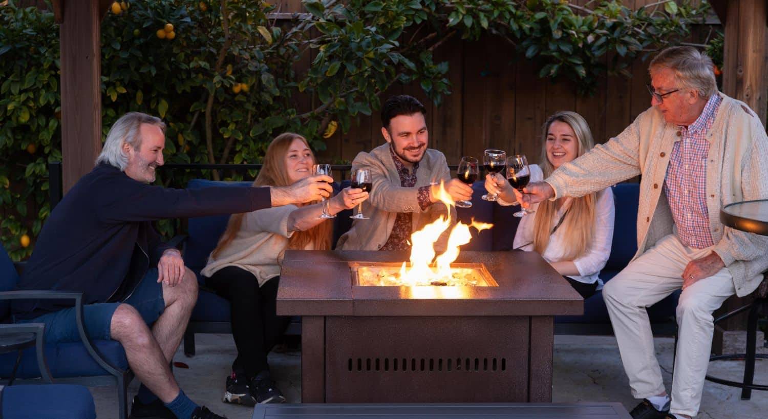 A group of men and women sitting and drinking wine at an outdoor firepit table